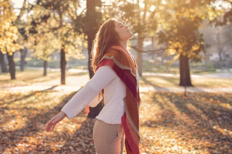 mujer con los brazos abiertos es un parque en otoño, feliz y con los ojos cerrados